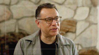 A man in glasses is standing in front of a stone wall.